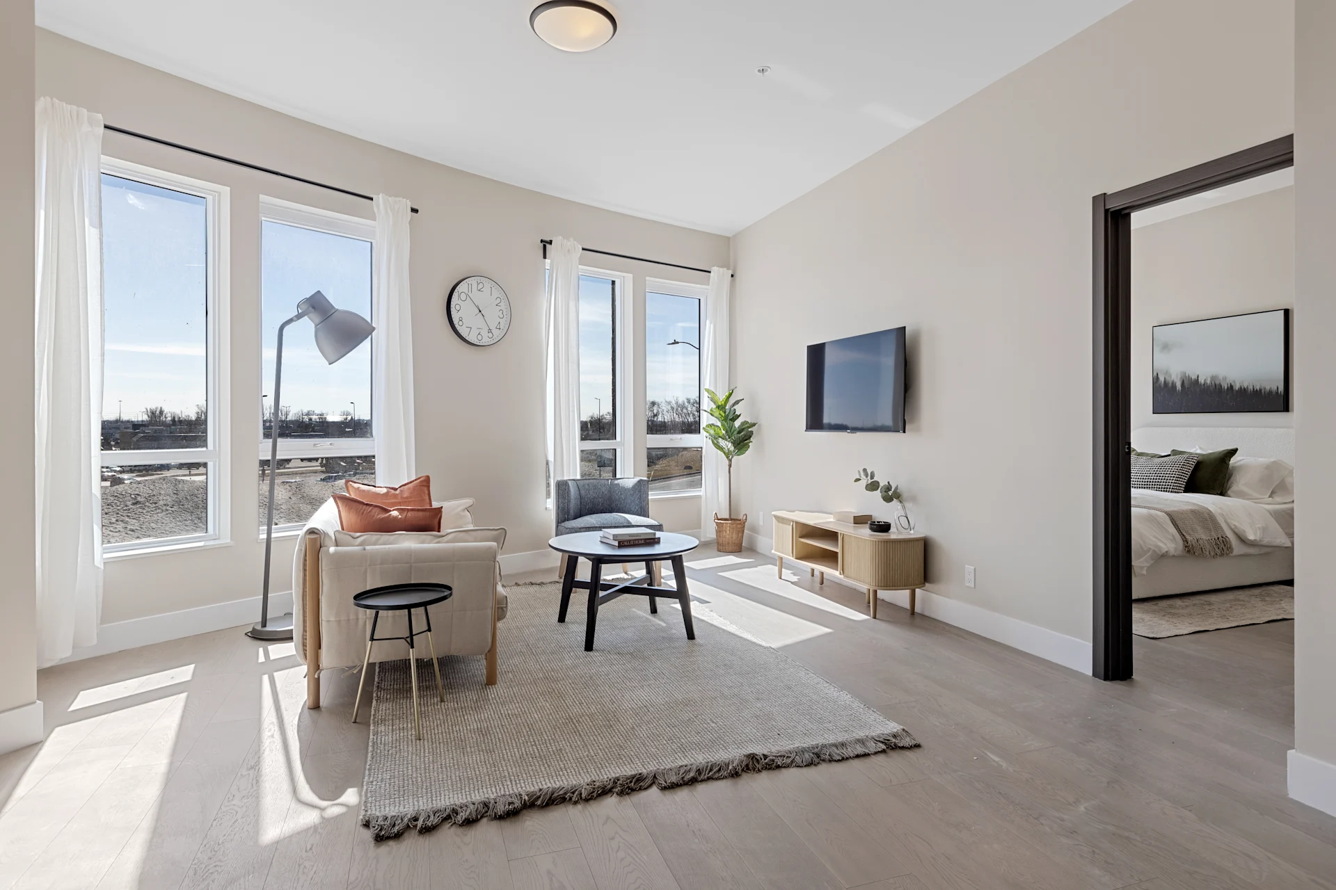 Sunlit living room in a model suite, looking out over the treeline